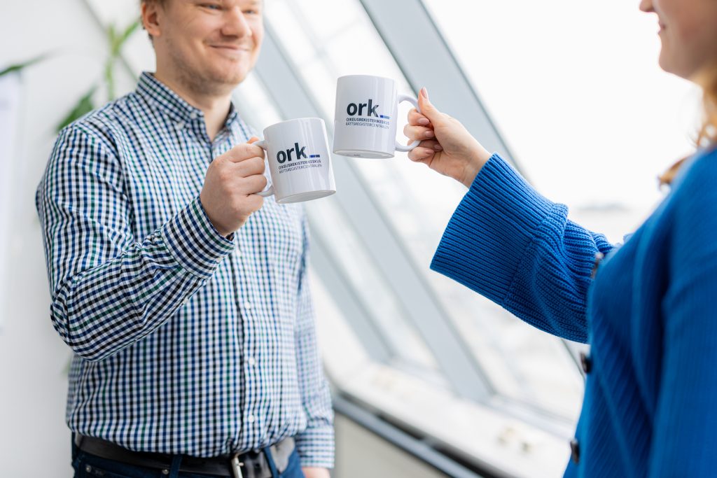 Kaksi ihmistä skoolaa mukeilla, jossa on ORK:n logo.
